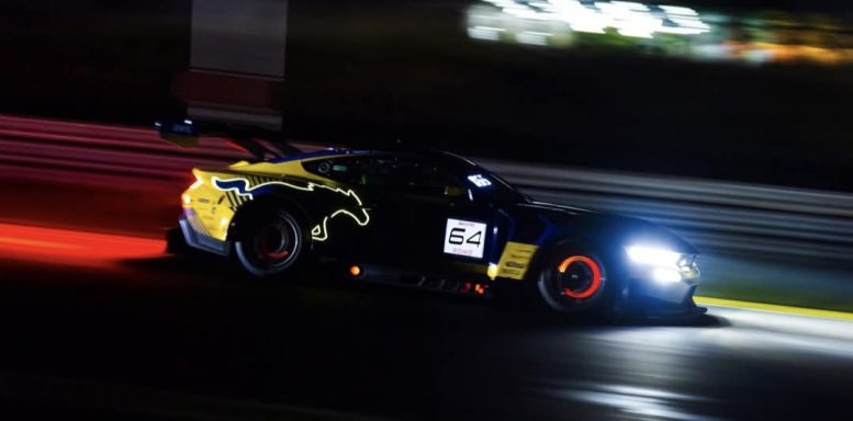 Ford Mustang GT3 Rennwagen mit gelber und schwarzer Lackierung fährt bei Nacht mit hellen Scheinwerfern.