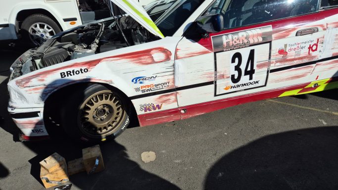 Reparaturen am Auto Rennwagen mit Startnummer 34, teilweise demontiert, steht auf einer Rennstrecke.