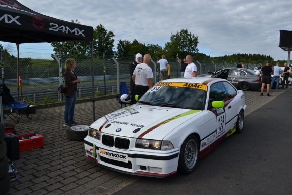 Track-Day-Vorbereitungen Rennwagen BMW M3, geparkt auf einer Rennstrecke, mit Zuschauern im Hintergrund.