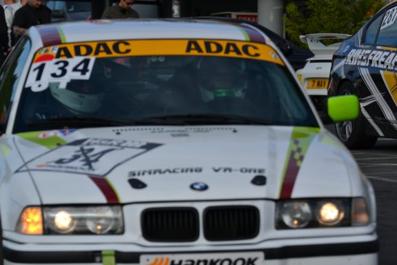 Frontansicht des Team-BMW Weißer BMW mit ADAC-Logo und Startnummer 134, parkt auf einem Eventgelände.
