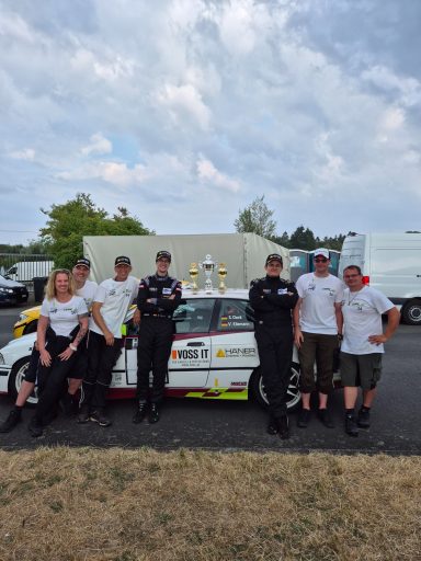 Das Team RingSpeed Gruppensfoto von sechs Personen vor einem Rennwagen mit Pokalen auf dem Dach.