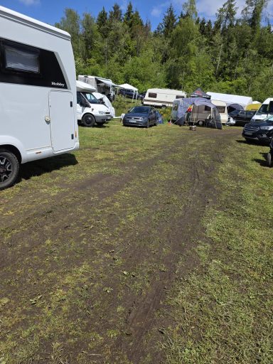 Etwas matschig Campingplatz mit Wohnmobilen und Autos auf einem schmalen, matschigen Weg umgeben von Bäumen.