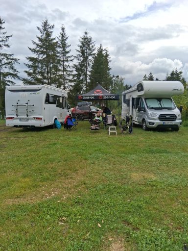 Renés Lager Zwei Wohnmobile stehen auf einer Wiese mit Bäumen im Hintergrund und Campingstühlen davor.