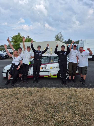 Das erfolgreiche Team RingSpeed Gruppe von Personen in Rennanzügen, feiert neben einem Rennwagen.